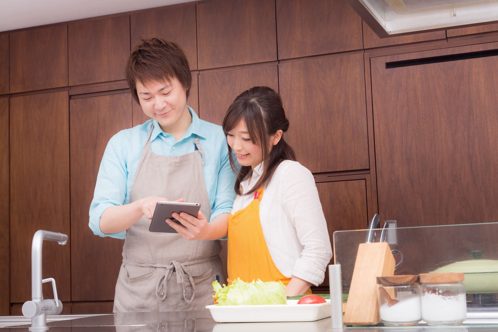 キッチンでタブレットを見ながらレシピを確認する夫婦［モデル：五十嵐夫妻］