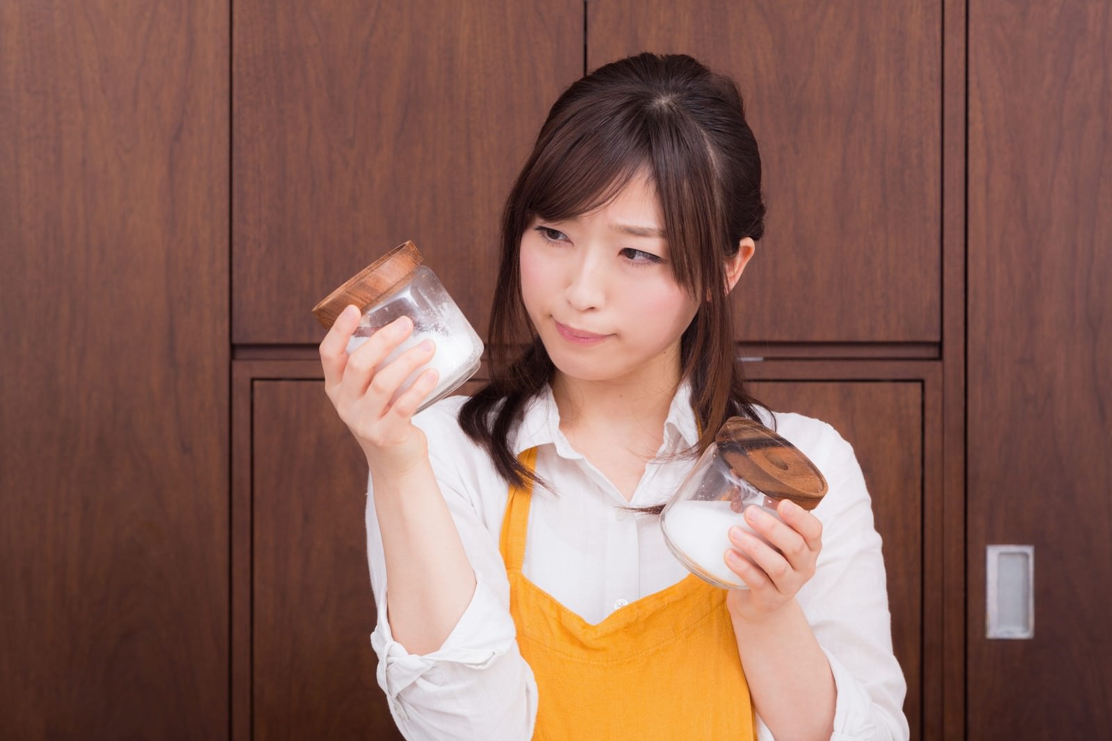 黄色いエプロンをした女性が調味料の瓶を持ち、中身を確認している様子［モデル：五十嵐夫妻］