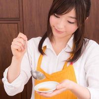 お玉でスープを味見する料理研究家の写真