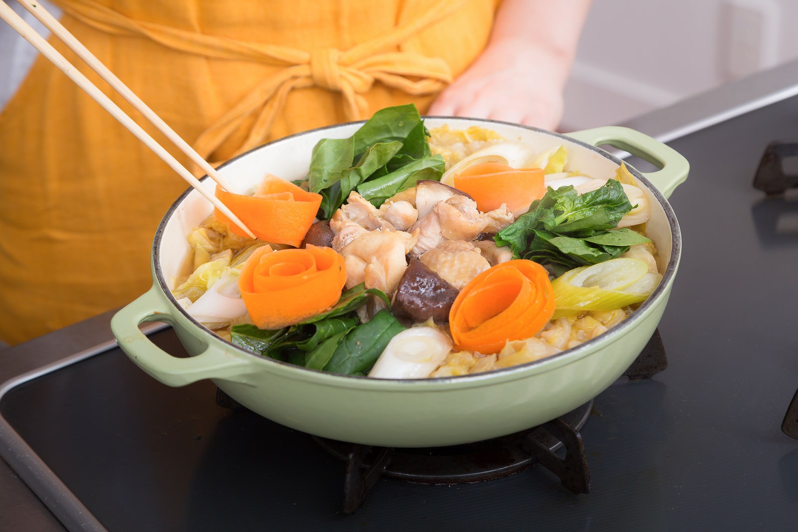 浅緑色の鍋に鶏肉と野菜が煮込まれており、箸で具材をすくう