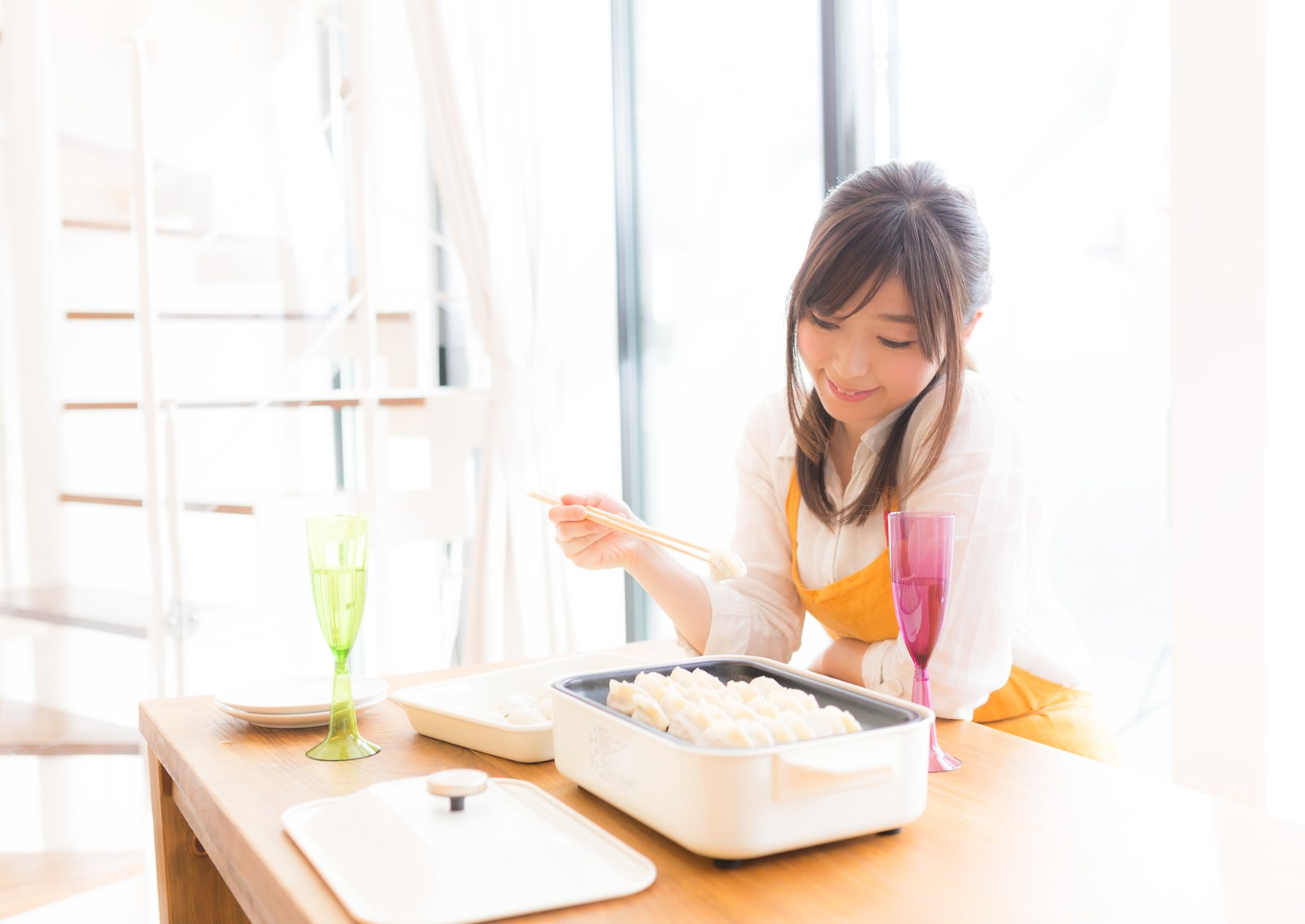 オレンジ色のエプロンを着けた女性がホットプレートで餃子を焼いている［モデル：五十嵐夫妻］