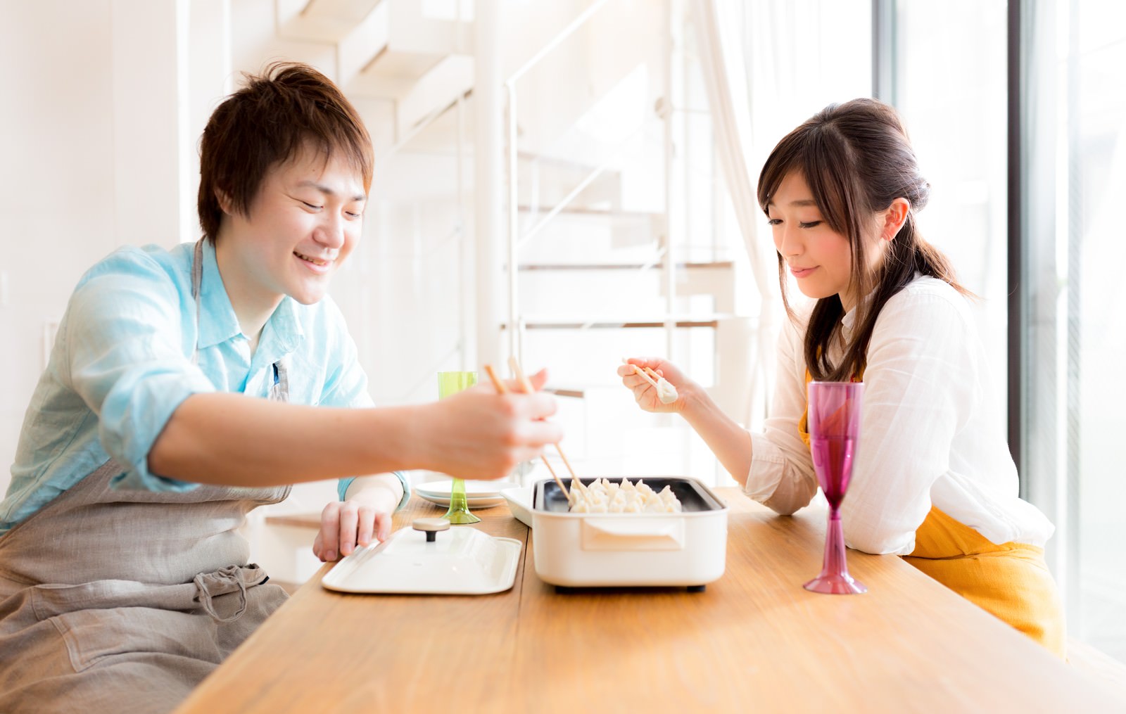 木のテーブルで餃子を味見するカップル［モデル：五十嵐夫妻］