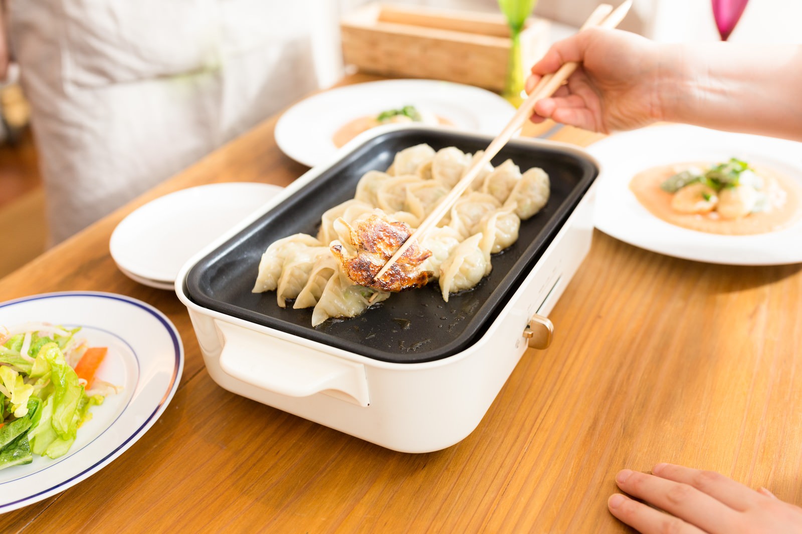 ホットプレートで焼いた焦げ目のついた餃子を箸でつまむ人の手［モデル：五十嵐夫妻］