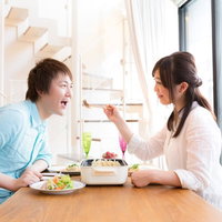 夫を餃子で餌付けする妻と喜ぶ夫の食卓風景の写真