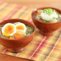 半熟卵とにんじんが入った木の椀の豚汁の写真