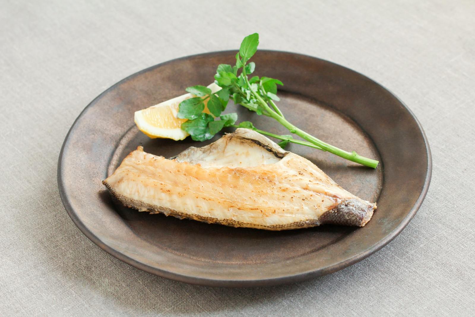 茶色の丸皿に焼き魚が盛られレモンスライスと緑の葉野菜が添えられている