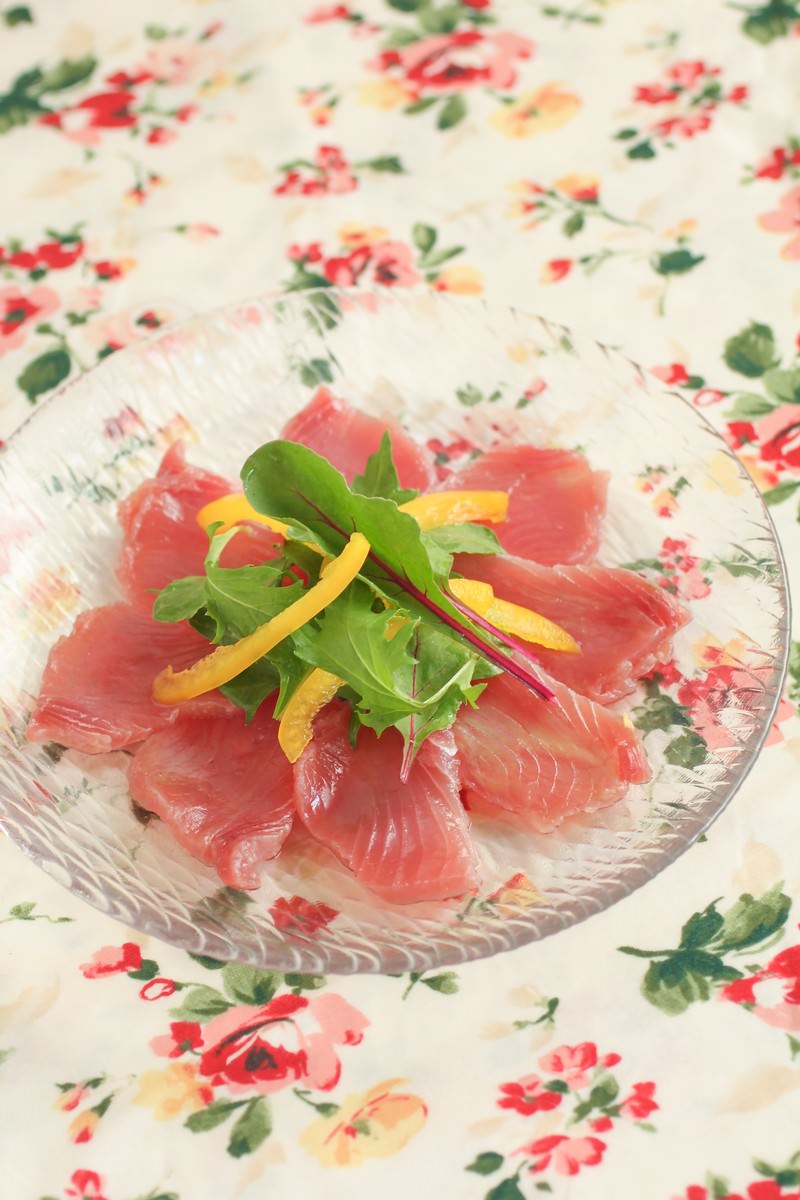 ガラス皿にピンク色のカツオの刺身が円形に並べられ中央に緑の葉野菜が乗っている