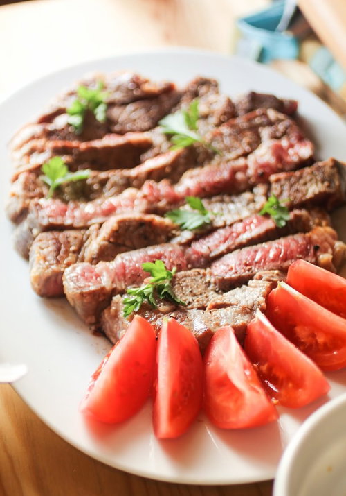 白い皿のステーキとトマトのくし切り