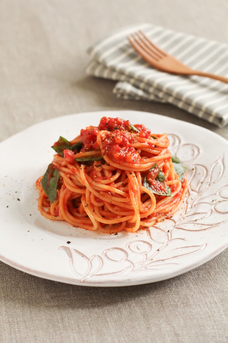 白い皿にトマトソースのパスタが盛られ緑の葉がトッピングされている