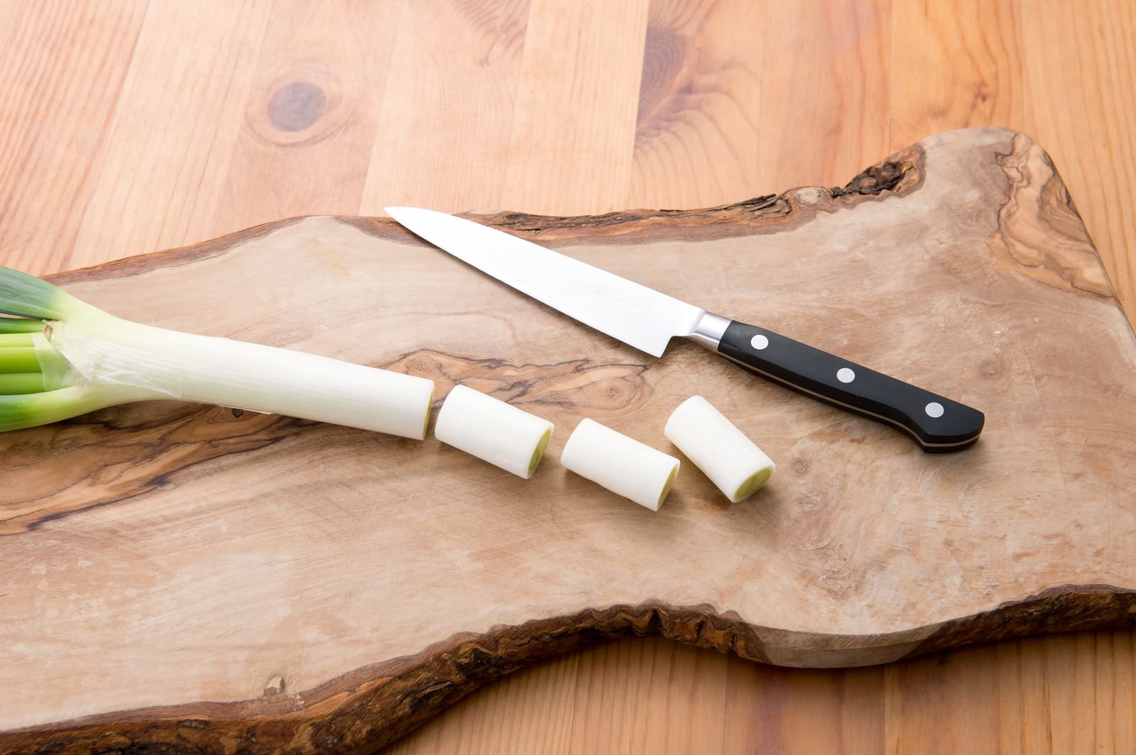 木製まな板の上に長ネギ1本と輪切りの数片が並び包丁が添えられている