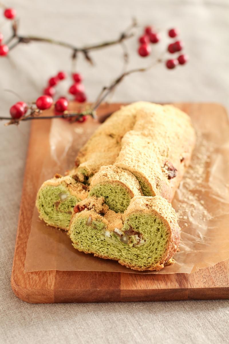木の板に緑の抹茶生地と白いクリームの渦巻きロールケーキが粉砂糖をまぶして置かれている