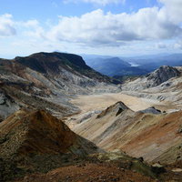 沼ノ平火口の荒れた地表と遠方の山並みの写真