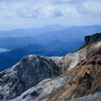 沼ノ平火口の荒涼とした地肌と遠景の山々、湖の写真