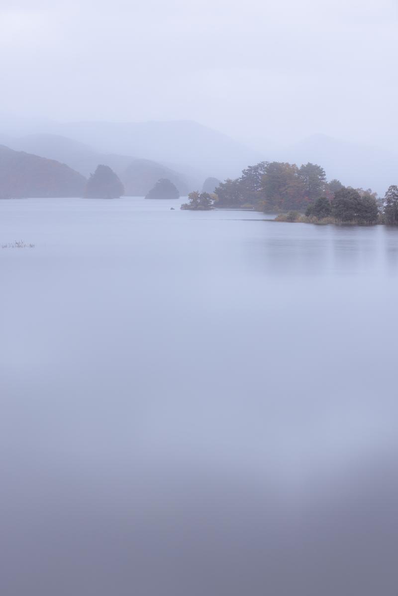 朝霧に包まれた秋元湖と紅葉した島々の朝の風景