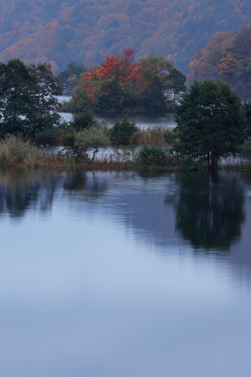 秋元湖の水面に映る秋色の樹木と遠くの山並み