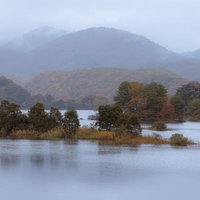 朝霧に包まれた秋元湖の穏やかな湖面と紅葉の山並みの写真