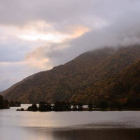 雲間から見える微かな朝焼け、紅葉に染まる秋元湖の写真