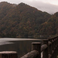 秋元湖の湖畔に立つ木製フェンスと紅葉山の秋景色の写真
