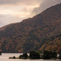 雲に隠れた焼けた空と秋元湖の紅葉に映る山並みの写真