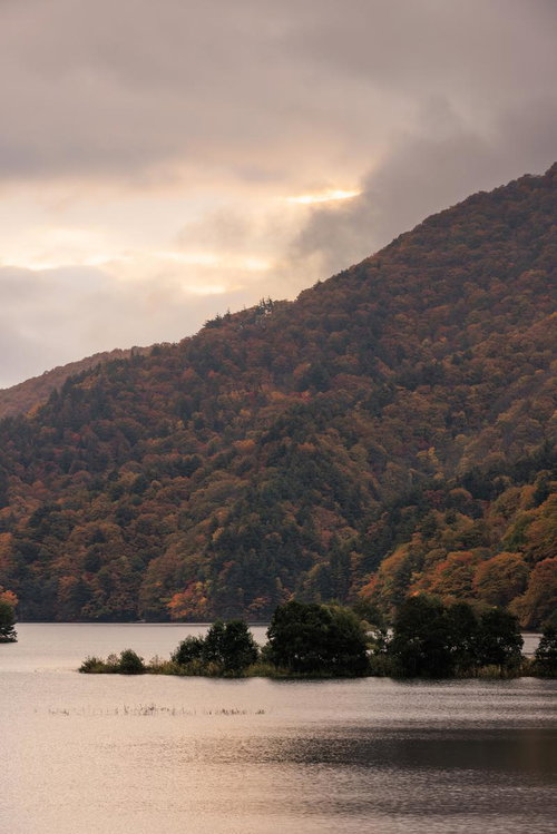 雲に隠れた焼けた空と秋元湖の紅葉に映る山並み