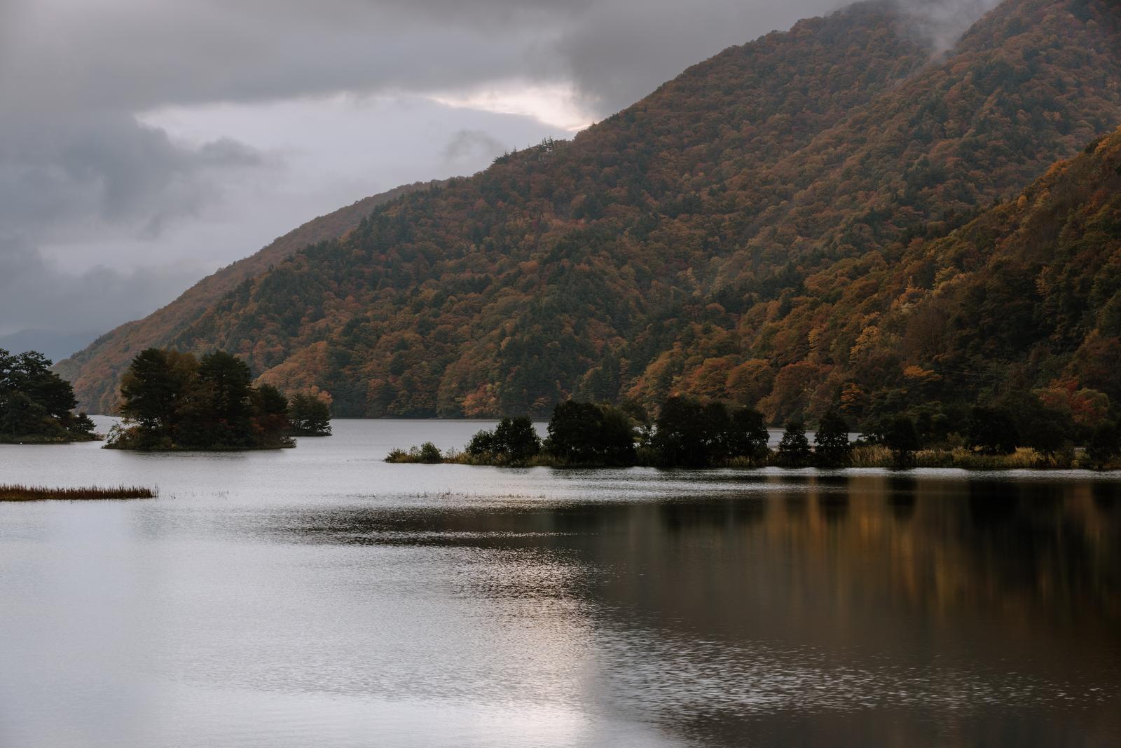 秋元湖の湖面に映る紅葉した山々と曇り空の風景