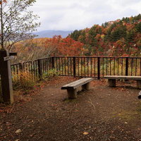 沼尻ルートの展望ベンチで眺める秋の紅葉と朝靄の山並みの写真