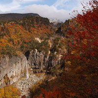 白糸の滝を囲む秋の断壁と紅葉、雪をかぶった山々の風景の写真