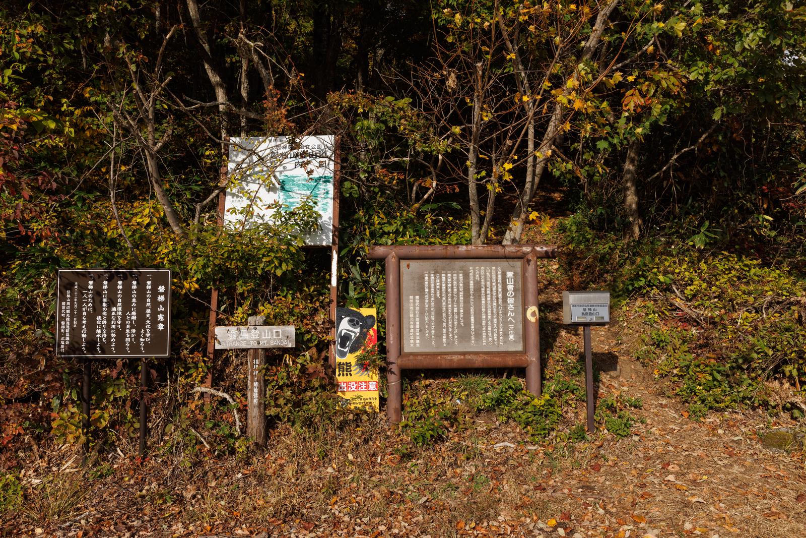 秋色の樹々に囲まれた磐梯山翁島登山口の木製看板と奥の湖景色
