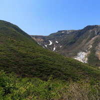 安達太良山の勢至平から眺める新緑と遠景の雪渓の写真