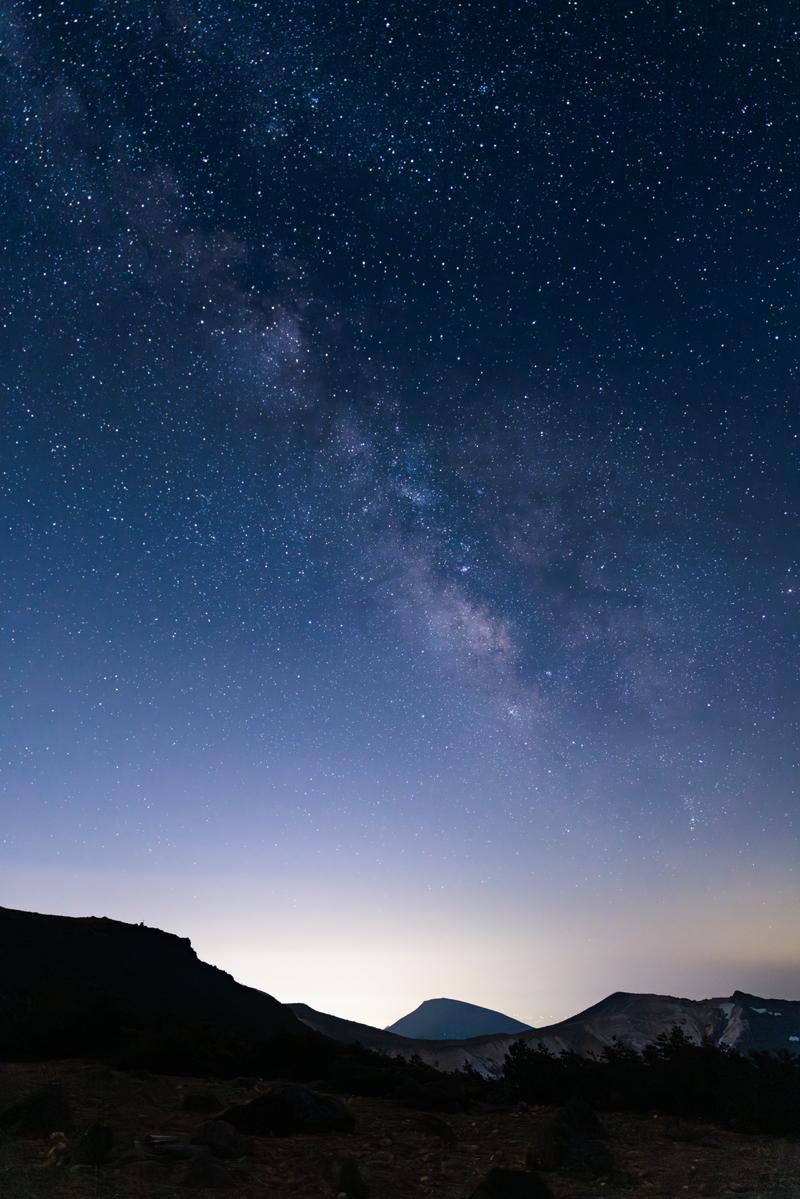 山並みのシルエットを背景に、天の川が輝く満天の星空の夜景写真