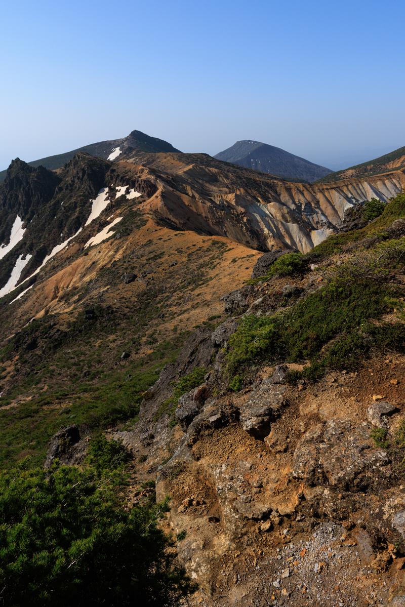 安達太良山と矢筈森の稜線、手前に新緑と露出した土、奥に複数の山峰が連なる