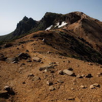 残雪が残る矢筈森の登山道と新緑の風景、火山地形の荒涼とした稜線の写真