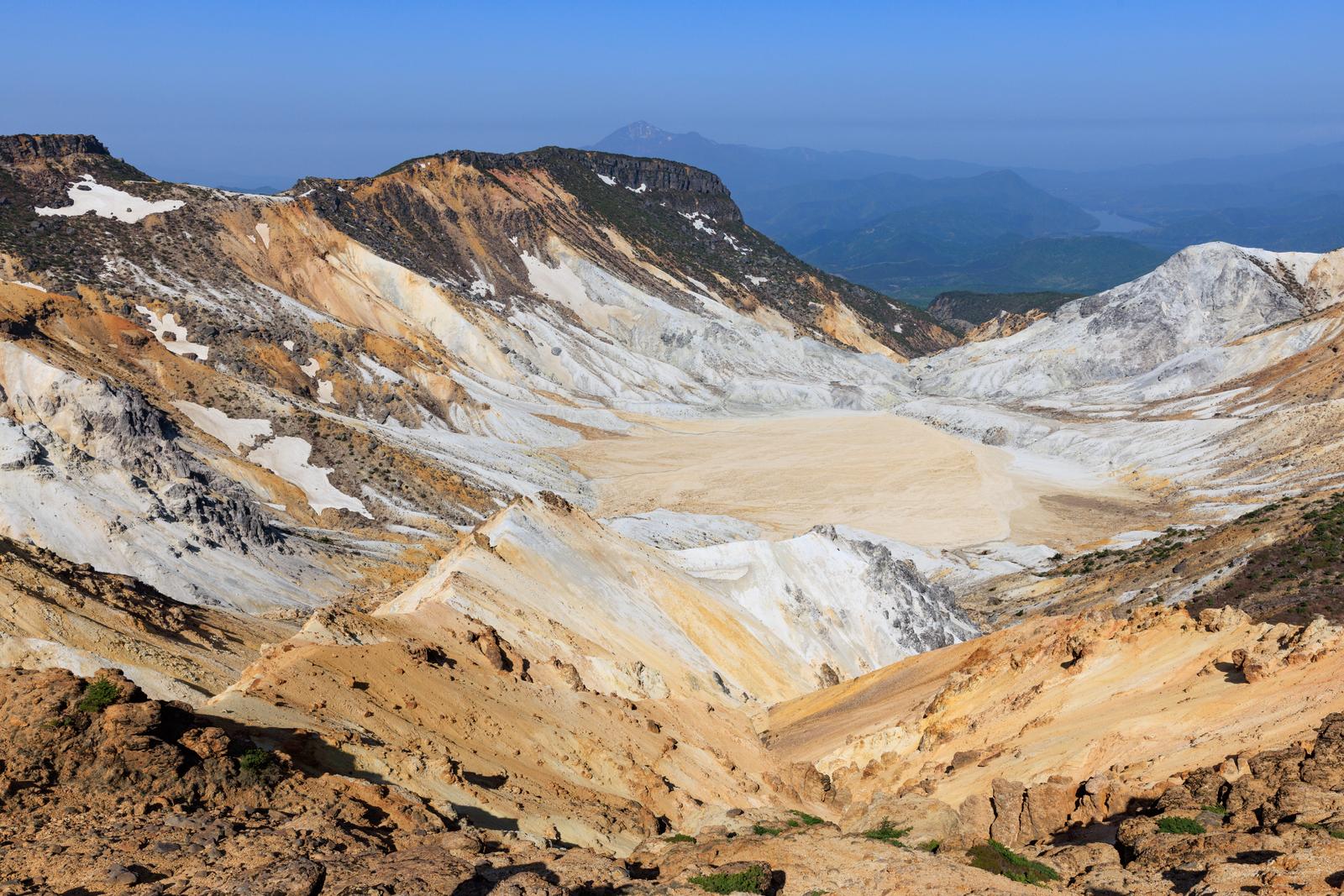 沼ノ平火口の白い硫黄地層と黄土色の荒涼とした斜面、遠景に秋元湖