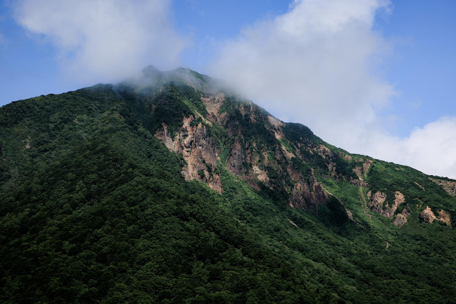 緑の樹林に覆われた磐梯山の山肌と雲がかかる山頂