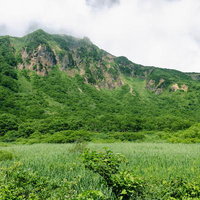 磐梯山猪苗代登山口から見る、山肌を覆う樹林と露出した岩壁の雄大な景観の写真