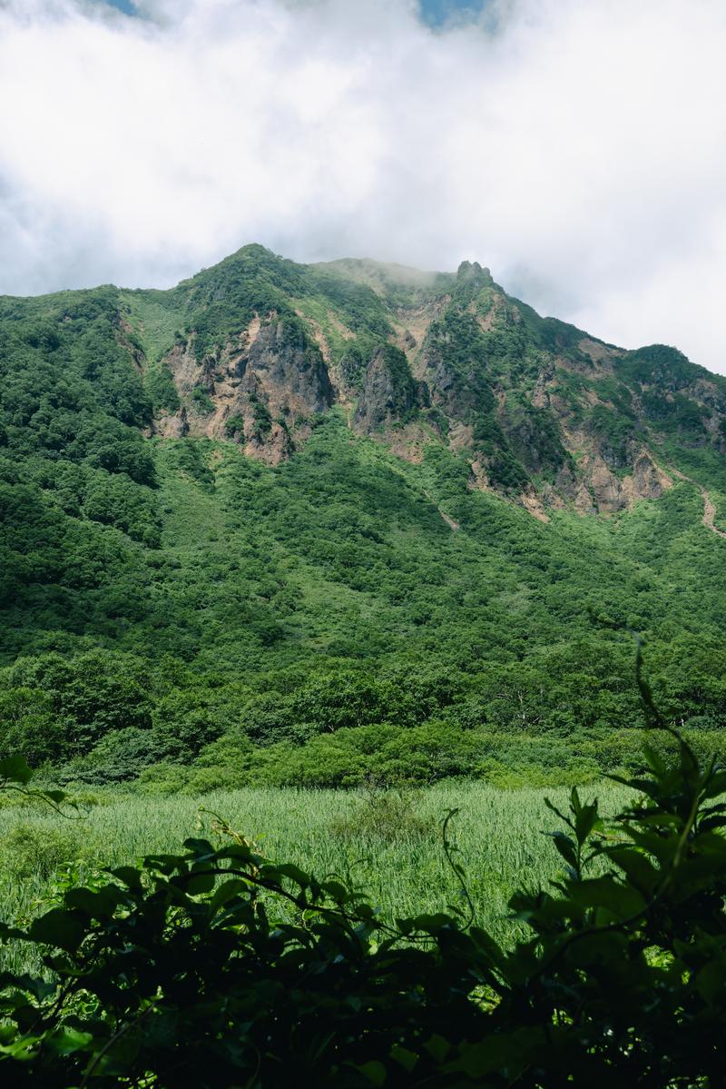 猪苗代町の登山口から見た、緑の山肌に露出した岩が見える磐梯山