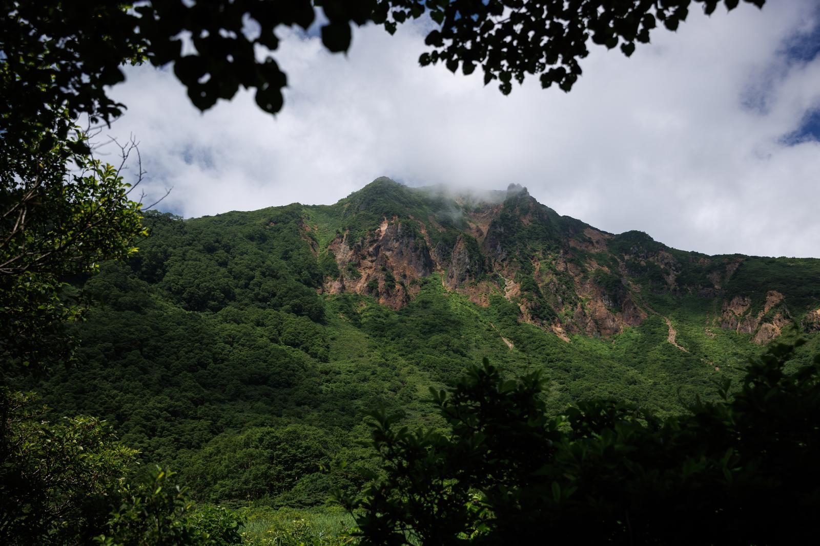 猪苗代登山口から見た磐梯山の山肌に樹木が茂り雲がかかった風景