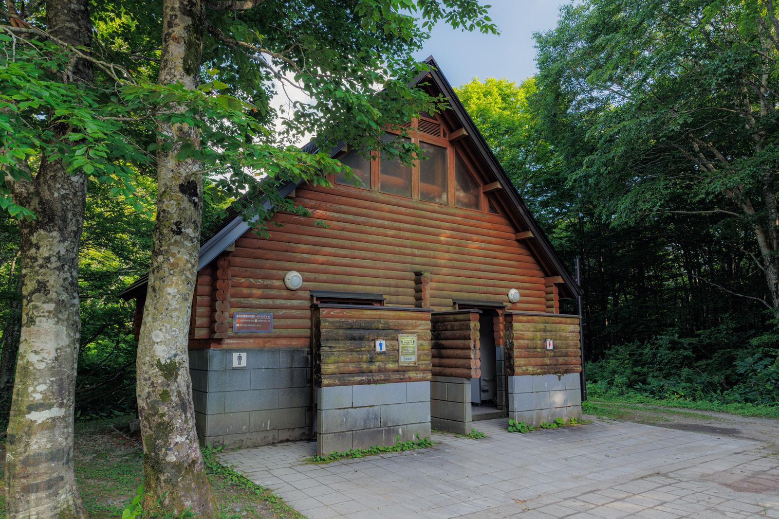 磐梯山八方台登山道の森に囲まれたログハウス造りのトイレ施設。樹木に囲まれ、石畳の広場がある