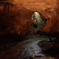 あぶくま洞の薄明りの通路と赤褐色の岩肌、鍾乳石の形成物の写真