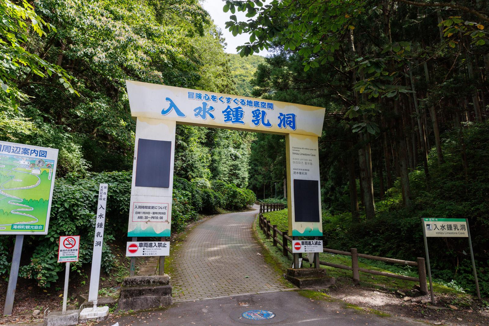 福島県の入水鍾乳洞入口に立つ白い案内板と石畳の通路を緑に囲まれて撮影