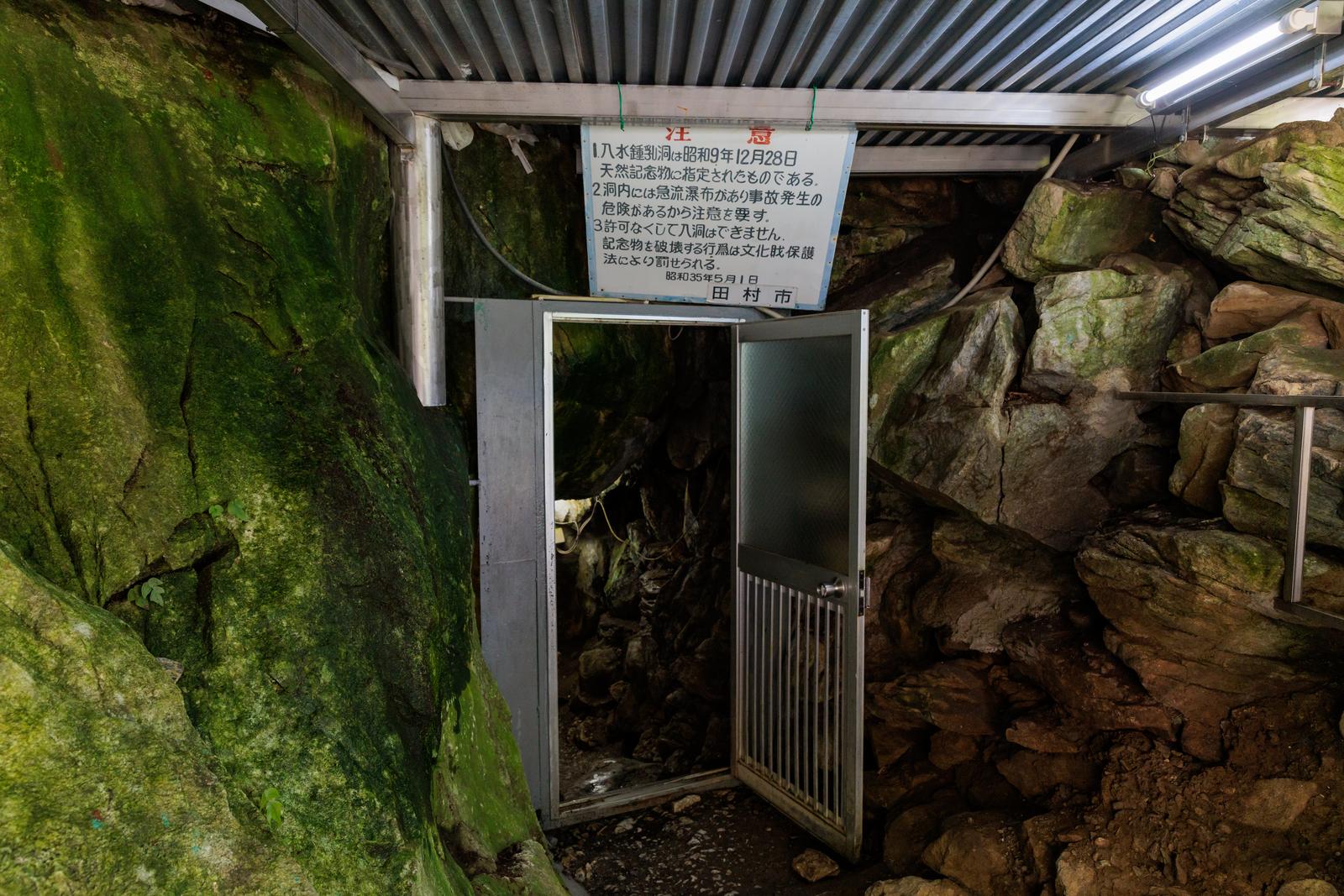 田村市の入水鍾乳洞の入り口に設置された金属製の扉と苔が生える岩壁