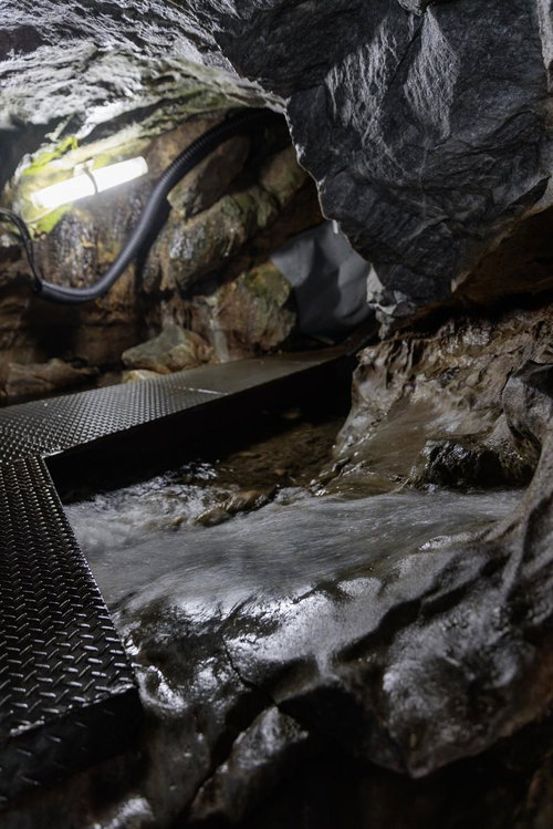 天井が低い入水鍾乳洞の洞内通路を歩く懐中電灯探検