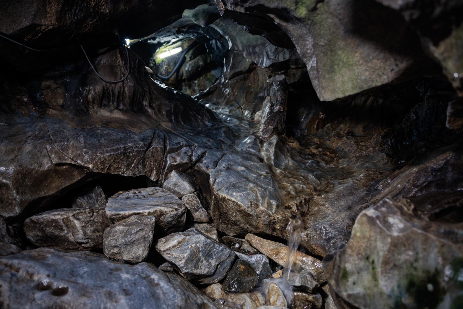 Underground water flowing on the rock walls of Nyūsui Stalactite Cave, with the cave interior illuminated by a flashlight.