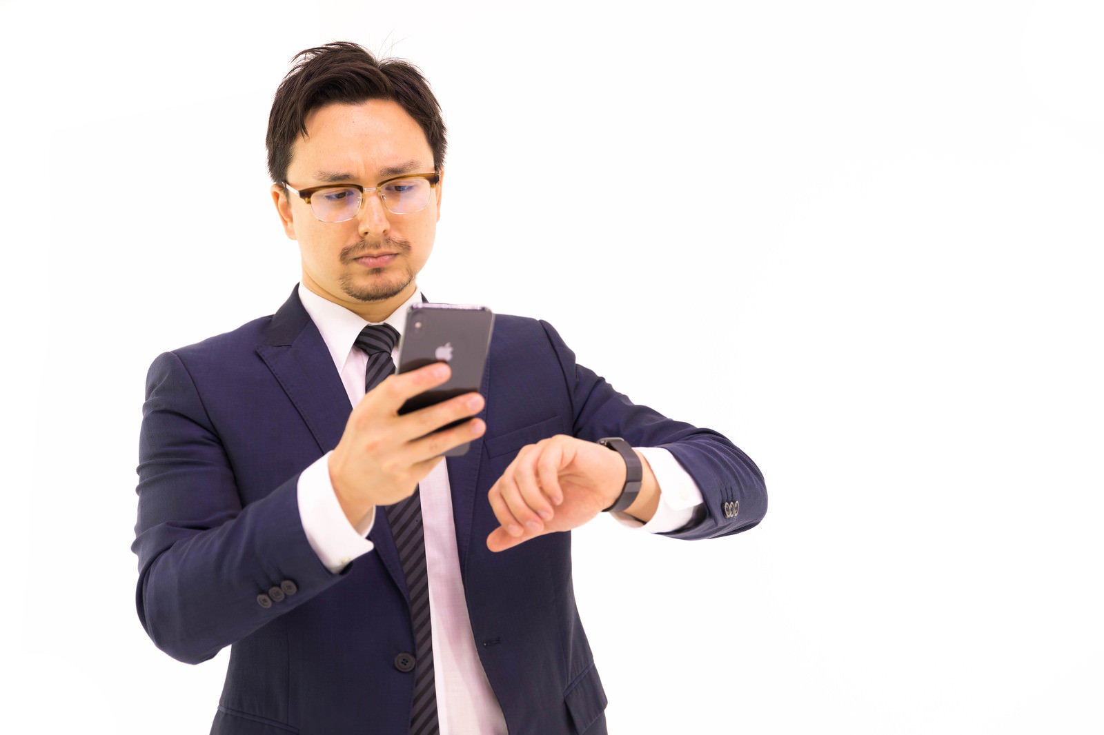 紺色のスーツを着た眼鏡の男性がスマートフォンとスマートウォッチを同時に操作している［モデル：Max_Ezaki］