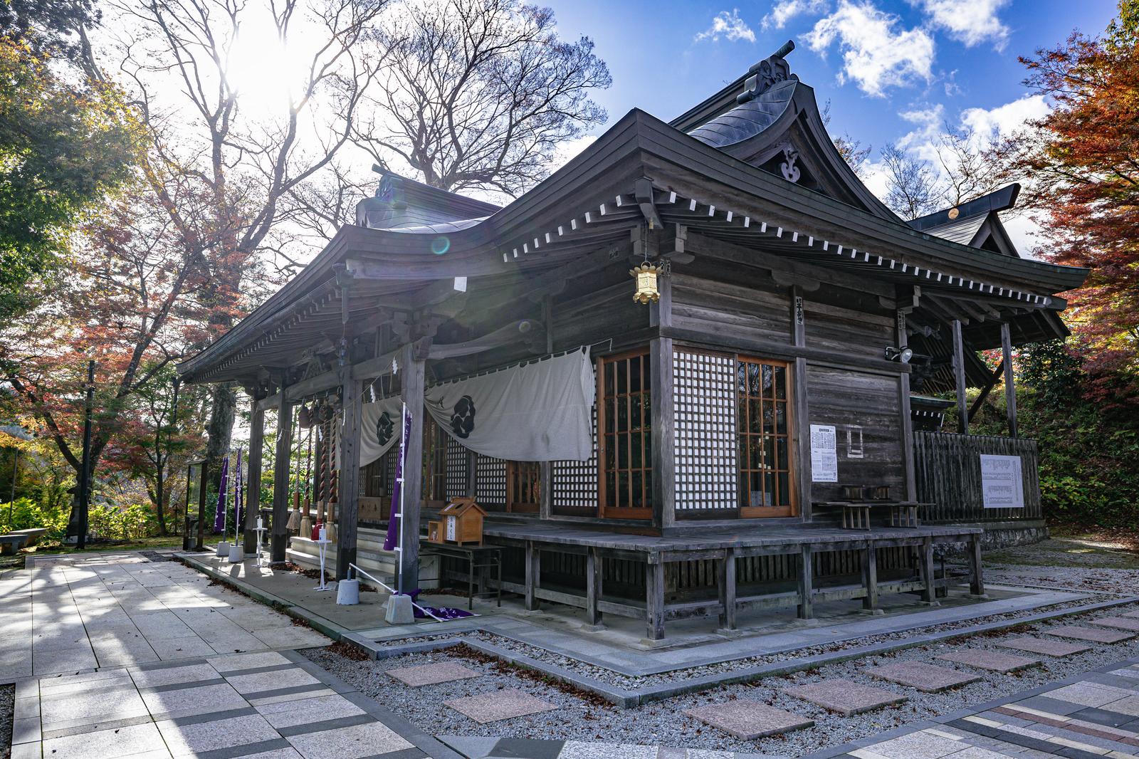 秋の紅葉に囲まれた黒い木造社殿の石都々古和気神社の参道