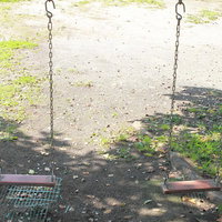 誰もいない公園に等間隔で並んだブランコの写真