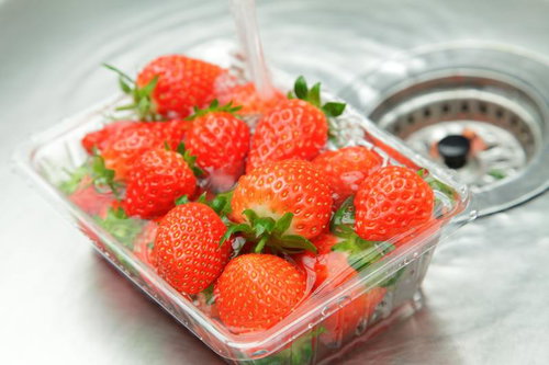 シンクでパックに入ったイチゴを洗う