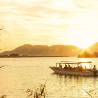 夕暮れの湖を進むボートと山のシルエットの写真