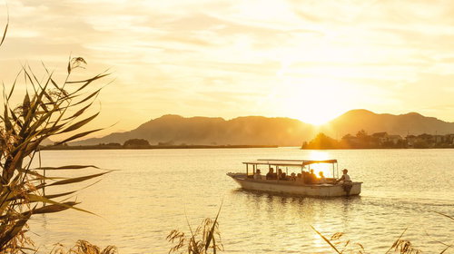 夕暮れの湖を進むボートと山のシルエット