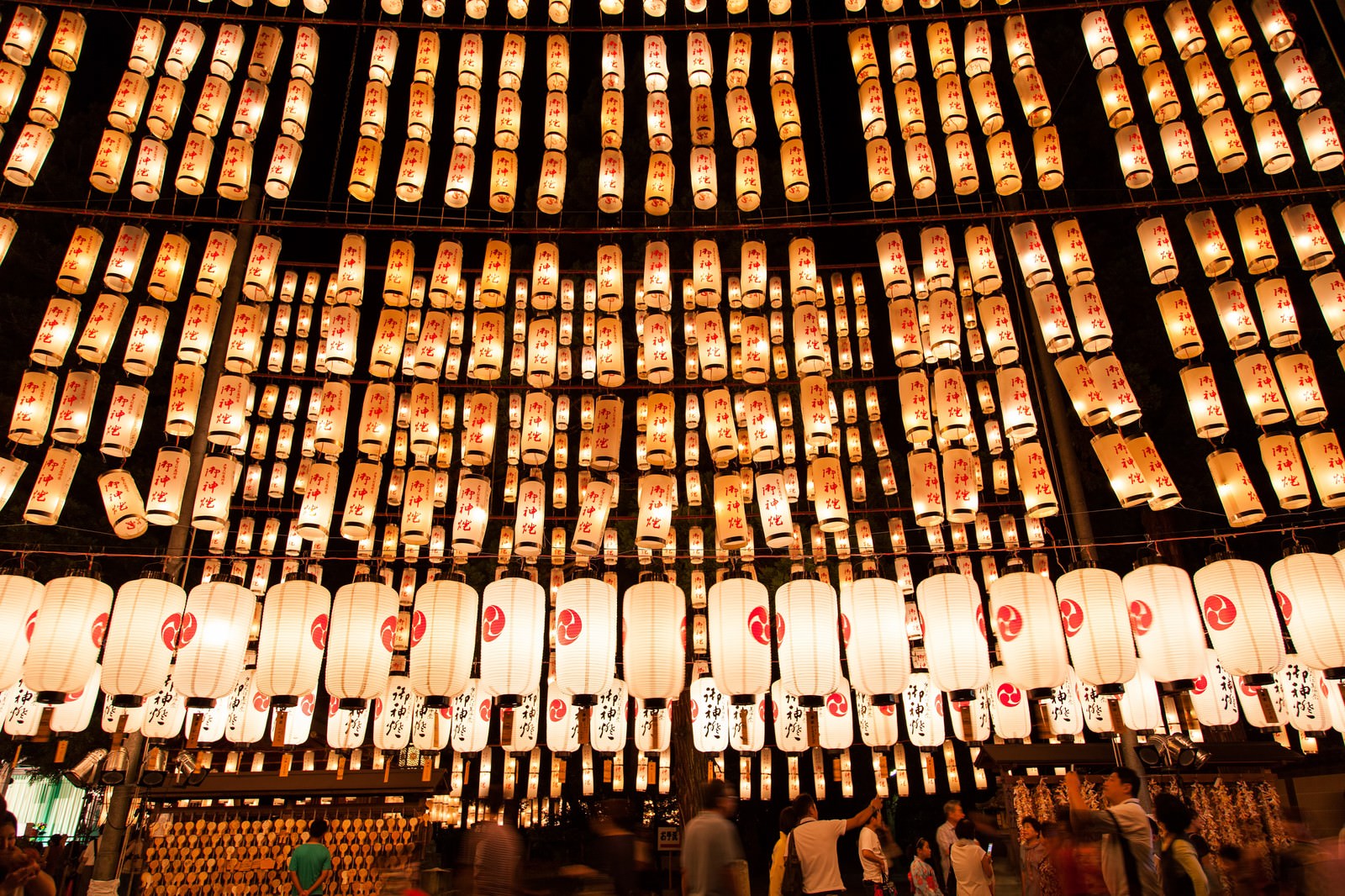 夜の軒下に並ぶ万灯祭のオレンジと白の提灯